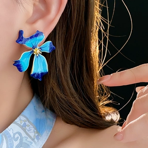 Detail view of model wearing vintage blue floral enamel earrings with elegant golden glow