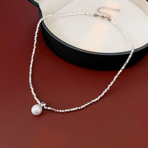 Detail of silver faceted bead necklace with white pearl and small crystal on red texture