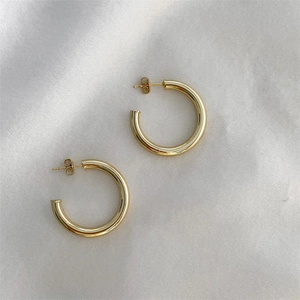 Detailed view of polished gold C-shape hoop earrings on elegant silk satin background