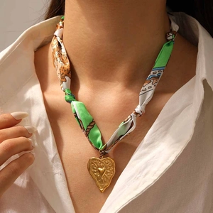 Gros plan d'un pendentif cœur vintage doré sur un collier en ruban imprimé vert