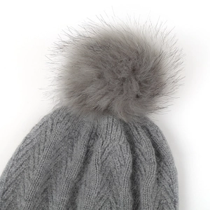 Detail of grey cable-knit beanie featuring a large fluffy faux fur pompom and soft texture