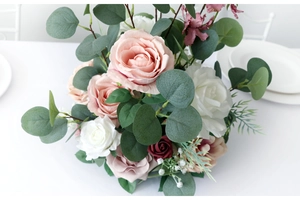 Detailed arrangement of white, pink and deep red silk roses with eucalyptus leaves on a table
