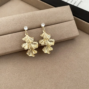 Close-up of golden ginkgo leaf earrings with clear zircon on brown velvet display