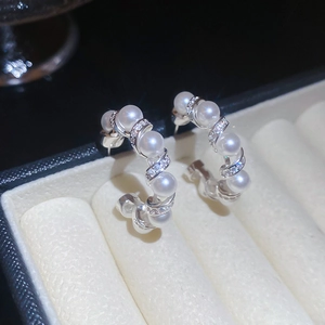 Macro shot of silver C-shaped pearl earrings with cubic zirconia in a jewelry box