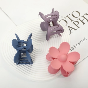 Three matte flower hair claws in pink, blue, and purple on a white ceramic tray