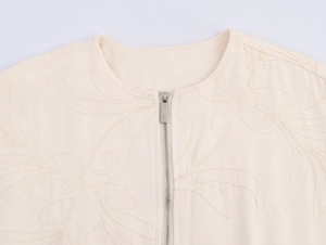 Close-up of beige casual jacket featuring delicate floral embroidery and metal zipper detail