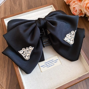 Close-up of black satin bow hair claw clip with triangle rhinestone accents on jewelry box
