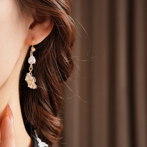 Detailed view of gold flower earrings with teardrop zircon on a model's ear