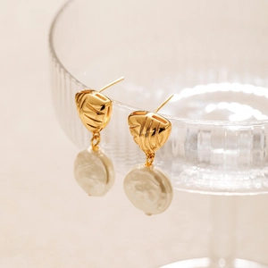 French pearl earrings with geometric gold triangle design hanging on a clear glass rim