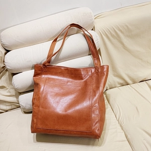 Détail d'un sac cabas vintage en cuir marron avec poche frontale posé sur un canapé beige