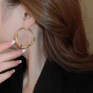 Close-up of model wearing large textured gold twist hoop earrings with a metallic finish