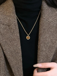 Détail d'une chaîne torsadée en or et d'un pendentif rond en œil de tigre sur modèle
