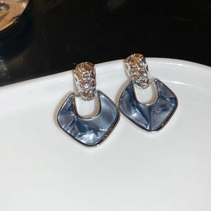Detail of silver textured stud earrings with grey acrylic shield pendant on ceramic tray
