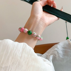 Detail view of gold-plated bracelet with pink floral beads and green center gem