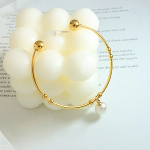 Golden open bangle with pearl pendant and metal beads on white bubble candle base