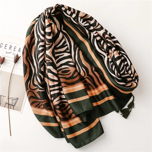 Detailed view of animal print scarf with green borders and delicate tassels on a white surface