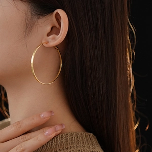 Close-up of a large gold hammered circle earring worn on a model against a black background