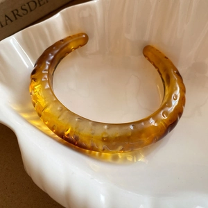 Vintage amber resin open cuff bracelet with embossed dotted texture on white plate