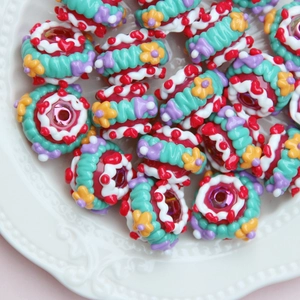 Macro detail of hand-painted colorful resin beads with floral patterns in a white tray
