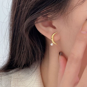 Close-up of a model wearing a gold moon-shaped stud earring with a white pearl detail
