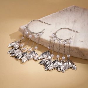 Detailed macro view of silver hoop earrings with faux pearl tassels and fish tail charms