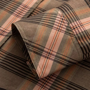 Macro detail of plaid shirt cuff showing fine texture and orange-brown woven fibers