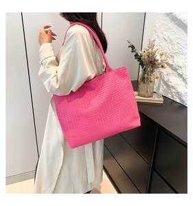 Side view of model wearing a large pink woven tote bag in a minimalist room
