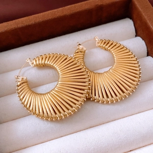Close-up of golden C-shaped hoop earrings with radial stripes and vintage fan design