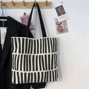 Detail of minimalist beige canvas tote bag with black vertical stripes hanging on a hook