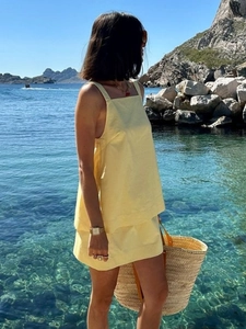 Pale yellow two-piece summer set with square neck top and mini skirt against ocean background