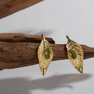 Detailed close-up of leaf-shaped gold earrings with oval green peridot gemstones on wood