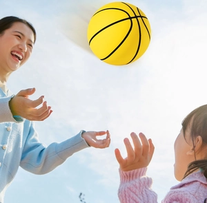 Outdoor shot of a mother and child playing with a vibrant yellow elastic rubber mini basketball