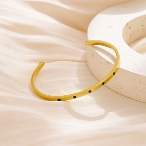 Detail of 18k gold plated bangle featuring inlaid blue crystals on a stone display