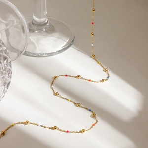 Detail of gold necklace with colorful beads on a white surface with glassware