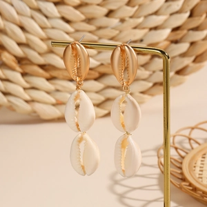 Detail of gold shell drop earrings with a triple-layered seashell design on a stand