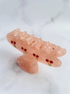 Close-up of pink marbled acetate hair claw clip with detailed 3D red cherry patterns