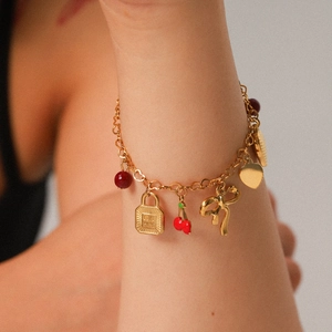 Gold charm bracelet with heart, cherry, and lock pendants on a woman's wrist