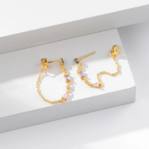 Elegant gold tassel earrings with colorful zircons on white minimalist geometric stand