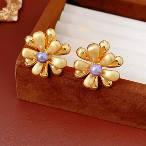 Macro view of 18k gold flower earrings with matte petals and a purple pearl center