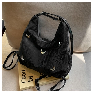 Detail of black wrinkled texture tote bag with silver butterfly charms on a sofa