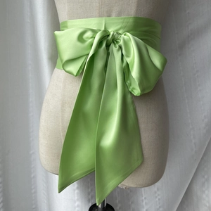 Gros plan d'une large ceinture obi en satin vert citron avec un grand nœud décoratif sur mannequin