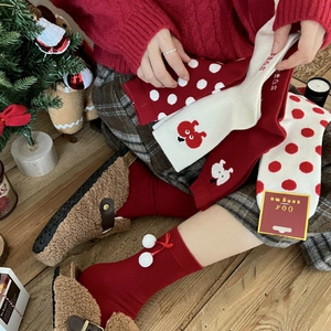 Thick festive Christmas socks with red knitting and pom-poms shown on wooden floor