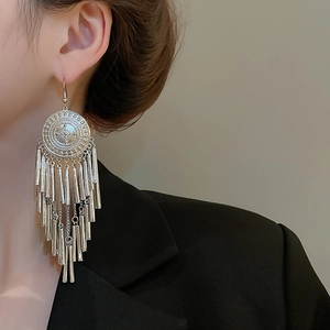 Detailed view of long silver tassel earrings with circular engraved discs on a model