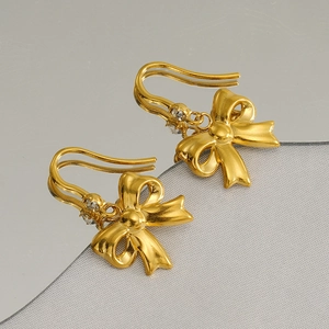 Boucles d'oreilles nœud doré élégantes avec cristaux sur fond miroir réfléchissant