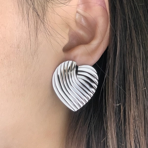 Détail macro d'une boucle d'oreille cœur argentée à texture ondulée sur un modèle