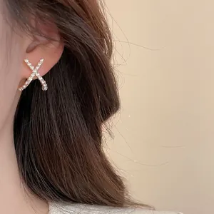 Nahaufnahme eleganter X-förmiger Goldohrringe mit glitzernden Kristallen am Modell