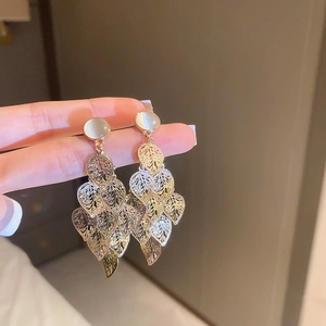 Detail of layered gold leaf earrings with white cat-eye stone held by fingers