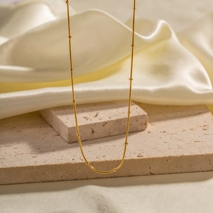 Detail of gold snake bone chain with metallic beads on soft white silk and stone texture
