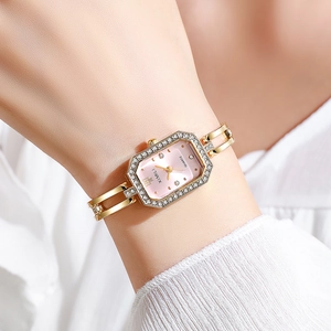Détail d'une montre carrée dorée avec lunette sertie de cristaux et bracelet à maillons