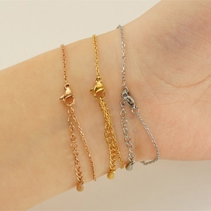 Détail de bracelets chaîne en or, argent et or rose avec fermoir mousqueton et pendentif goutte